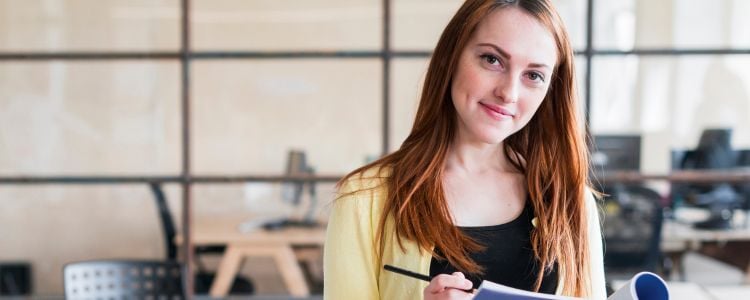 Mujer sosteniendo un lápiz en una libreta en su lugar de trabajo llevando su aprendizaje experiencial