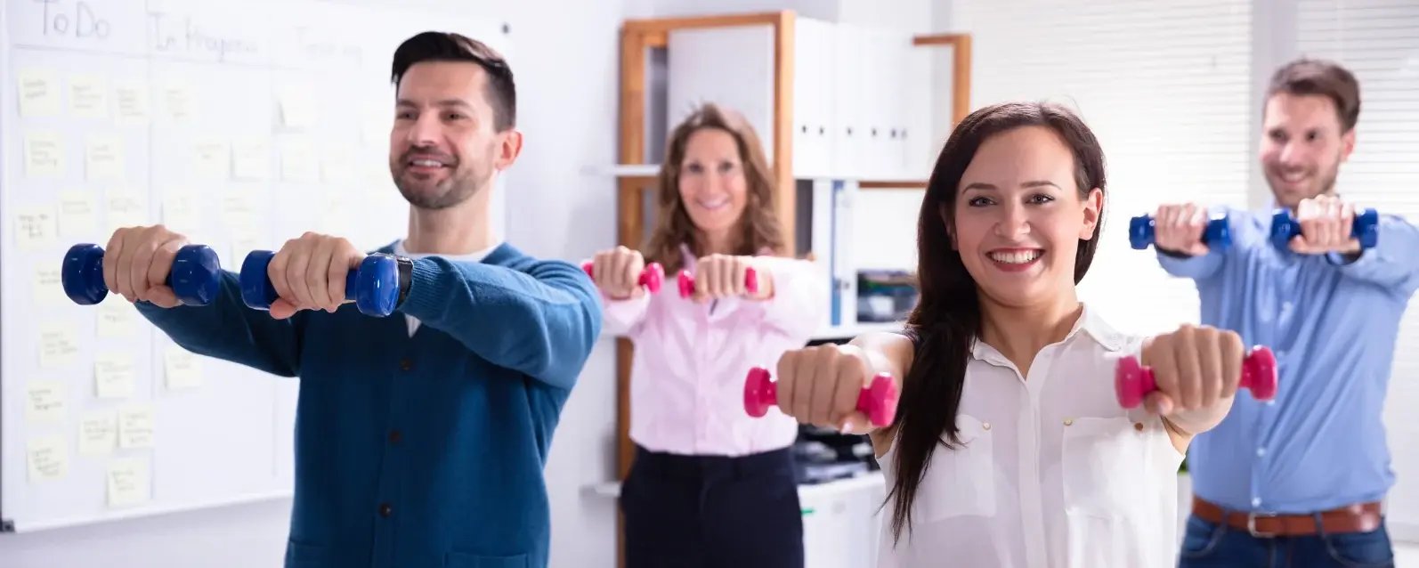 Trabajadores haciendo una rutina de ejercicio con pesas impartida por un coach de deportes